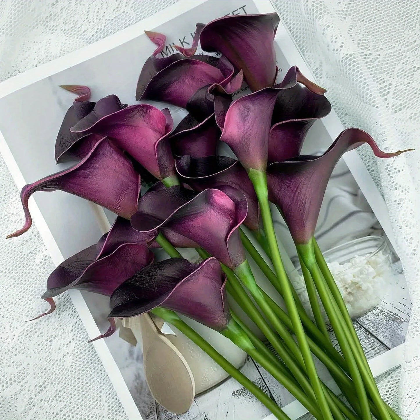 Dark purple artificial calla lily flowers bouquet on white surface