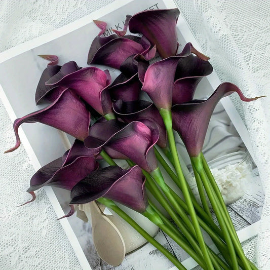 Dark purple artificial calla lily flowers bouquet on white surface