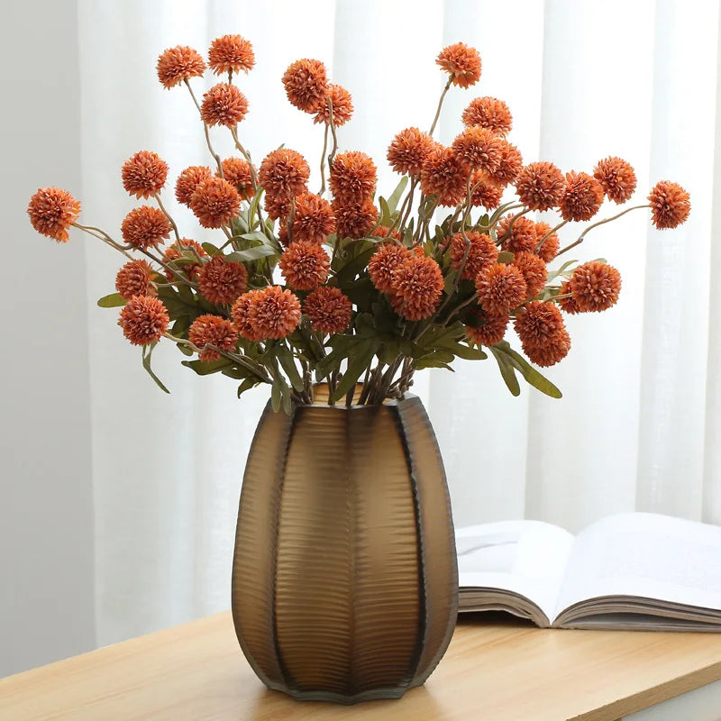 Orange artificial dandelion stems in bronze vase